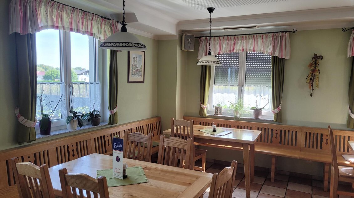 Ein gemütlicher Gastraum mit Holzstühlen und Tischen. Große Fenster lassen viel Licht herein und bieten einen Blick auf die Außenseite. | © TV Südsteiermark - Irene Löschnig