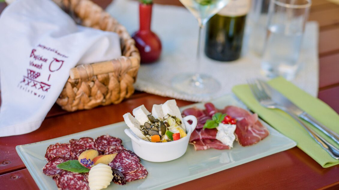 Ein schön angerichteter Teller mit verschiedenen Wurstsorten und Käse. Dazu ein Glas Wein und eine Flasche auf dem Tisch. | © Familie Repolusk | Weingut Repolusk