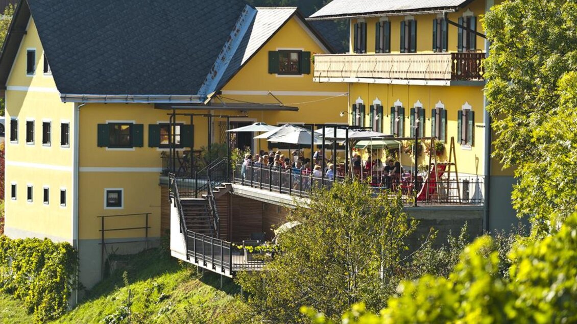 Ein gelbes Gebäude mit mehreren Fenstern und einem Balkon. Auf der Terrasse sitzen Menschen und genießen die Aussicht. | © Familie Repolusk | Weingut Repolusk