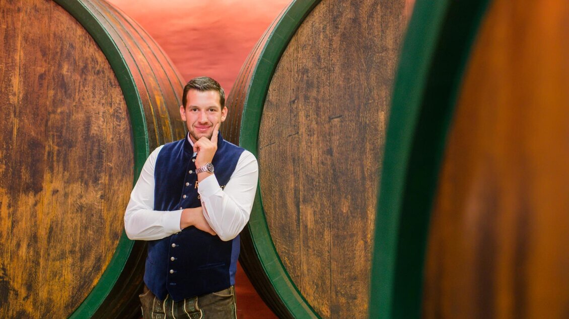 Ein Mann steht zwischen großen Holzfässern in einem Weinkeller. Er trägt traditionale Kleidung und hat eine nachdenkliche Pose. | © Familie Repolusk | Weingut Repolusk