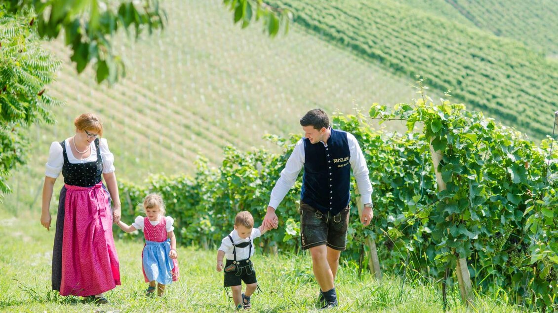 Eine Familie geht durch ein malerisches Weinfeld. Die Erwachsenen tragen traditionelle Kleidung, während die Kinder fröhlich mitgehen. | © Familie Repolusk | Weingut Repolusk