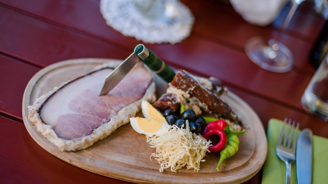 Ein schön angerichteter Teller mit Fleisch, frischen Salaten und einer Limettenscheibe. Der Teller liegt auf einem Holztisch. | © Familie Repolusk | Weingut Repolusk