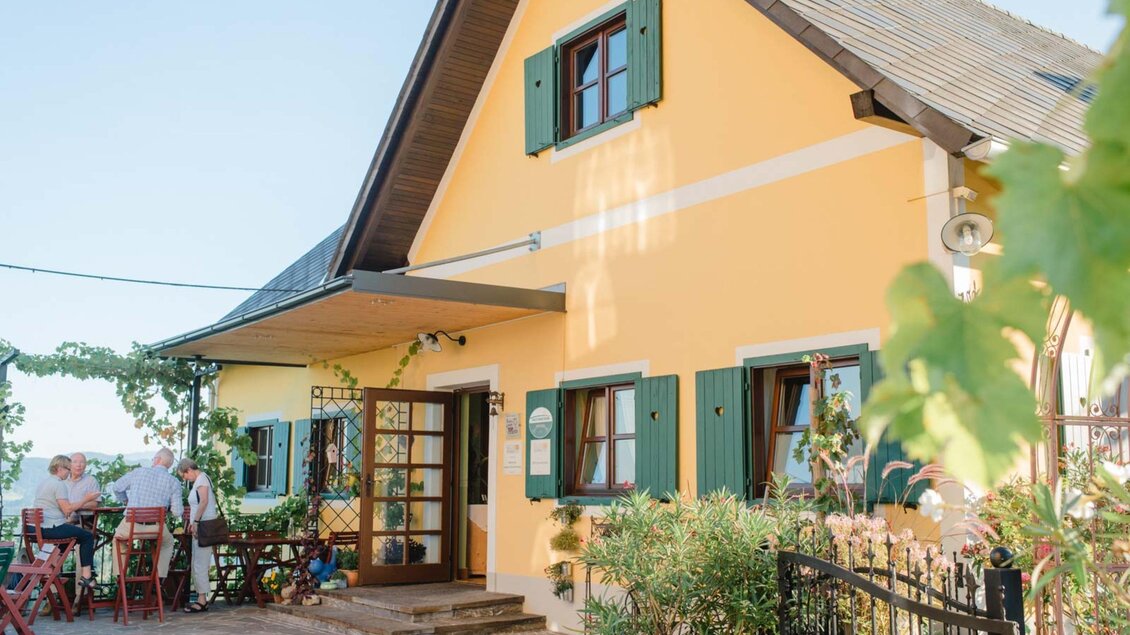 Ein charmantes, gelbes Haus mit grünen Fensterläden. Vor dem Haus sind Tische und Stühle, die zum Verweilen einladen. | © Familie Repolusk | Weingut Repolusk