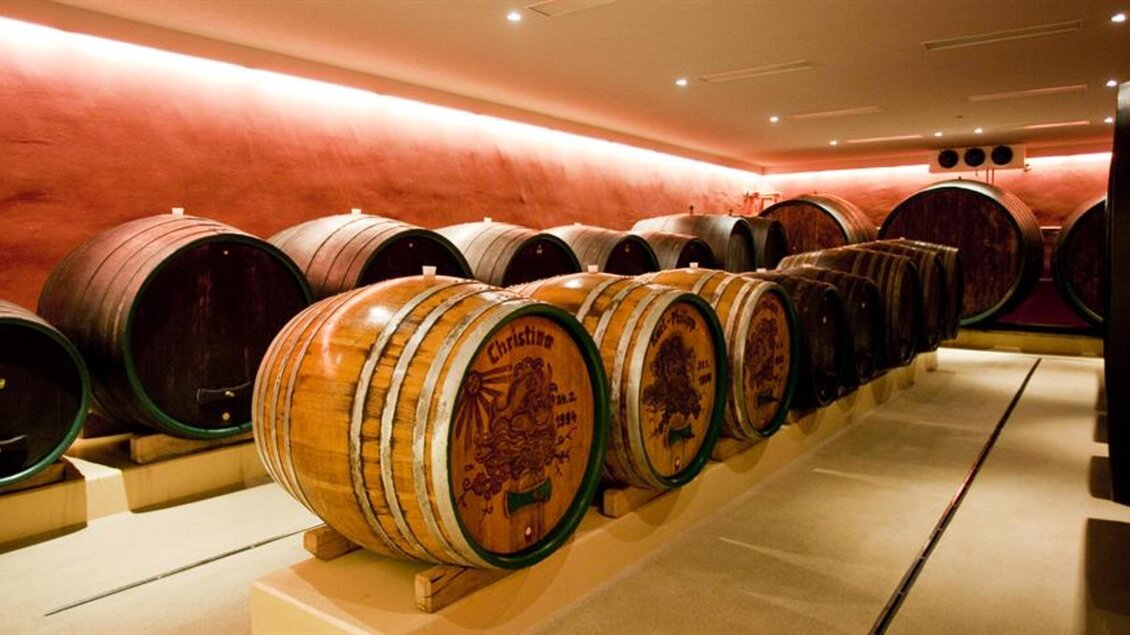 Ein Weinkeller mit mehreren großen Holzfässern. Die Wände sind in einem warmen Farbton gehalten und die Beleuchtung ist sanft. | © Familie Repolusk | Weingut Repolusk