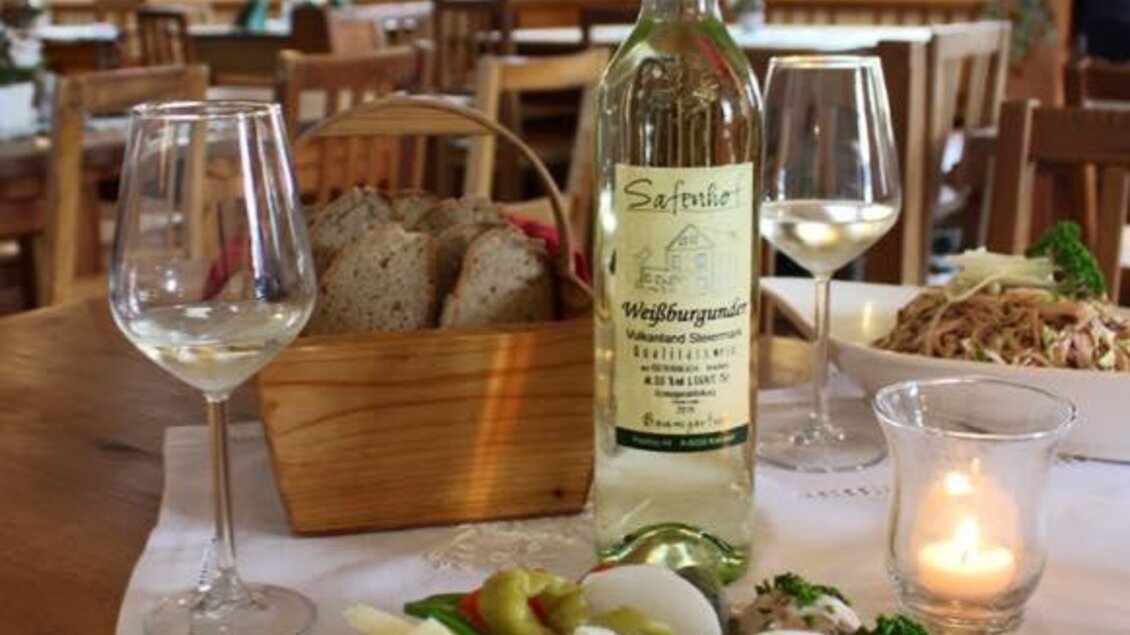 Ein rustikales Restaurant mit Holzstühlen und Tischen. Auf dem Tisch steht eine Platte mit Wurst und Käse, dazu eine Flasche Wein und Weingläser. | © Oststeiermark Tourismus