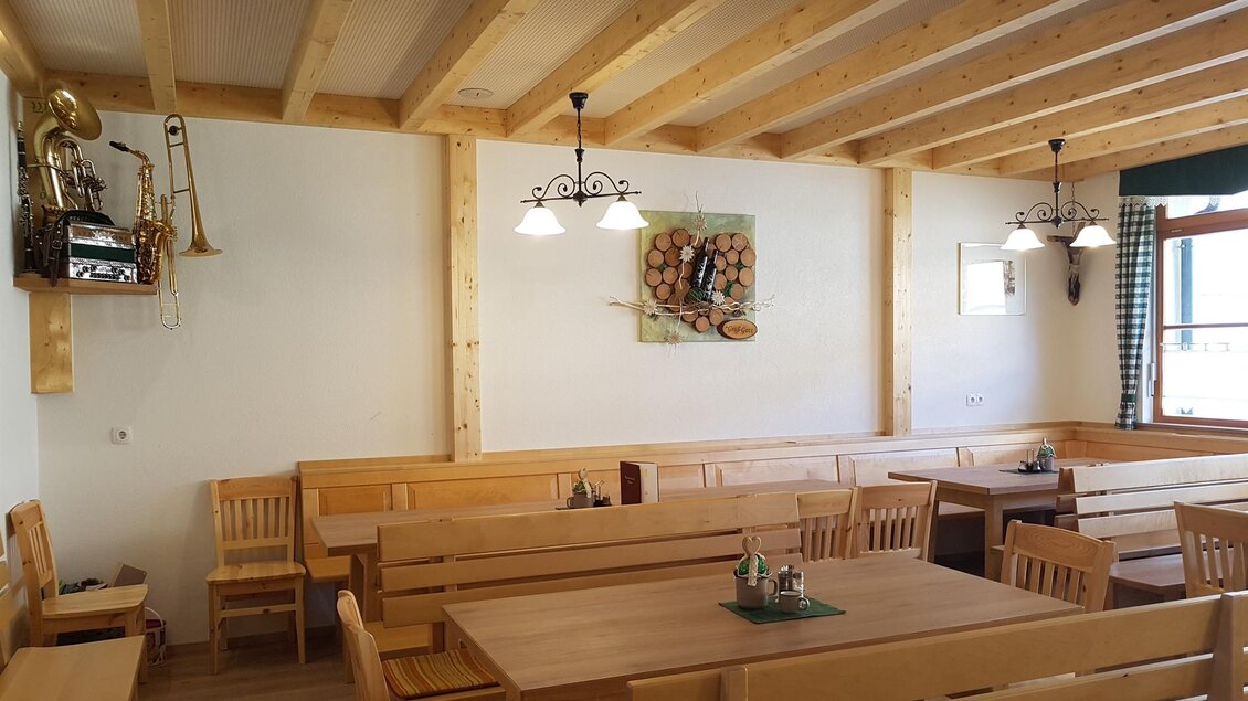 Ein gemütlicher Raum mit Holzmöbeln und einer warmen Atmosphäre. An den Wänden hängen Bilder und in der Decke sind Lampen installiert. | © Buschenschank Safner