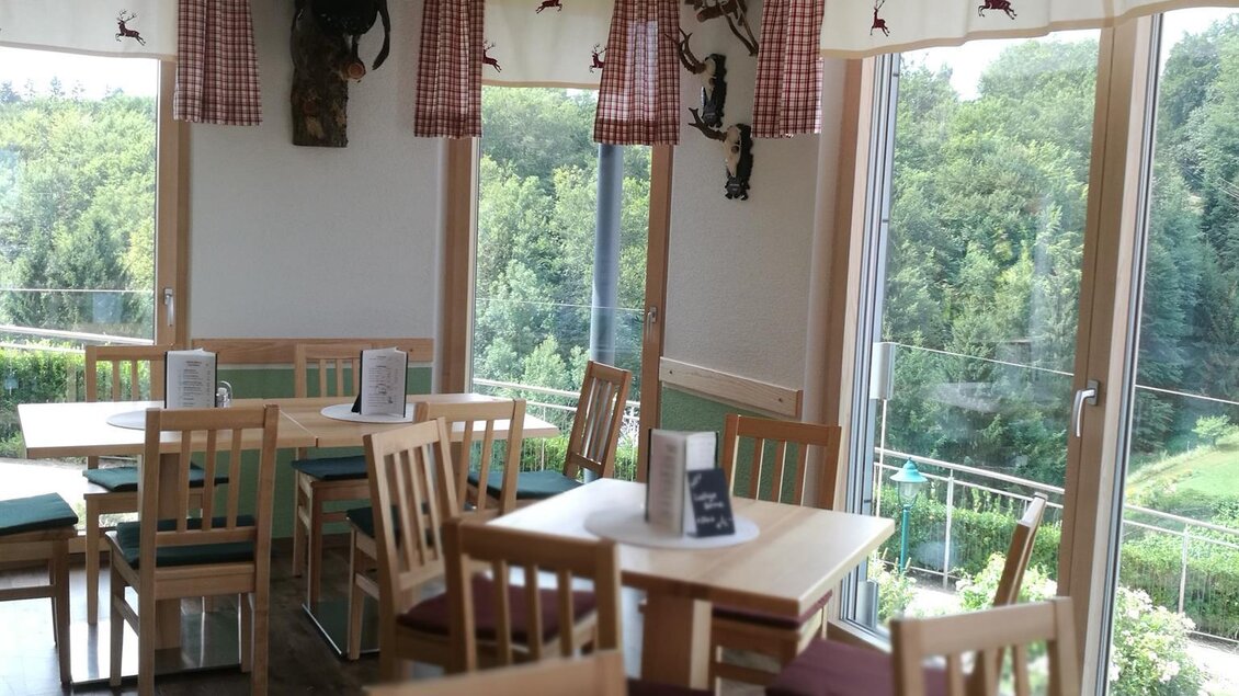 Ein gemütliches Restaurant mit Holztischen und Stühlen. Große Fenster bieten einen Blick auf die grüne Umgebung. | © Steiner