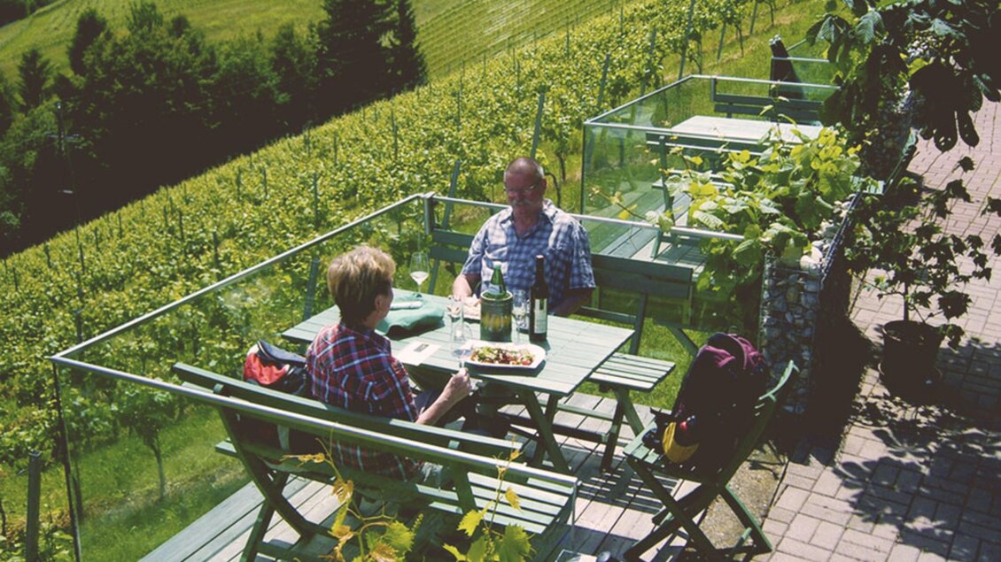 Gemütliches Essen im Freien mit Blick auf die Weinberge. Zwei Personen sitzen an einem Tisch und genießen eine Mahlzeit. | © Familie Sternat | Weingut Sternat