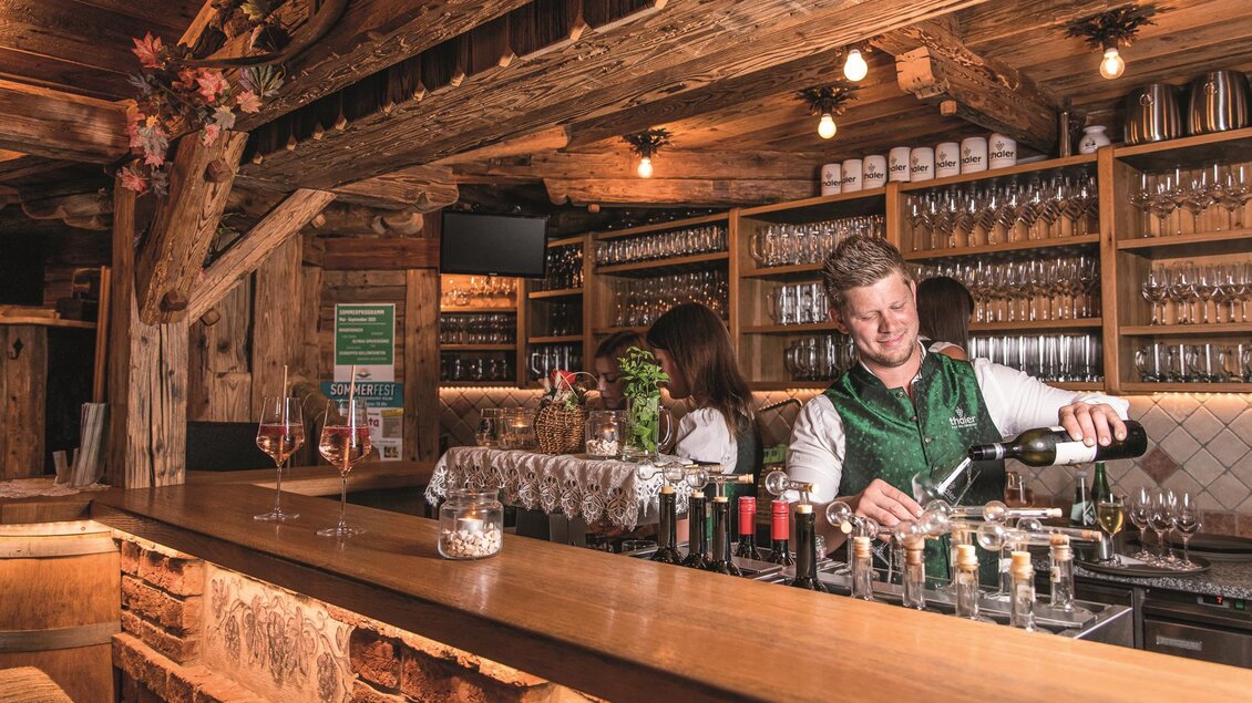 Eine gemütliche Bar mit Holzdekor und vielen Gläsern im Hintergrund. Ein Barkeeper serviert Getränke und sorgt für eine einladende Atmosphäre. | © Michaela Pfleger