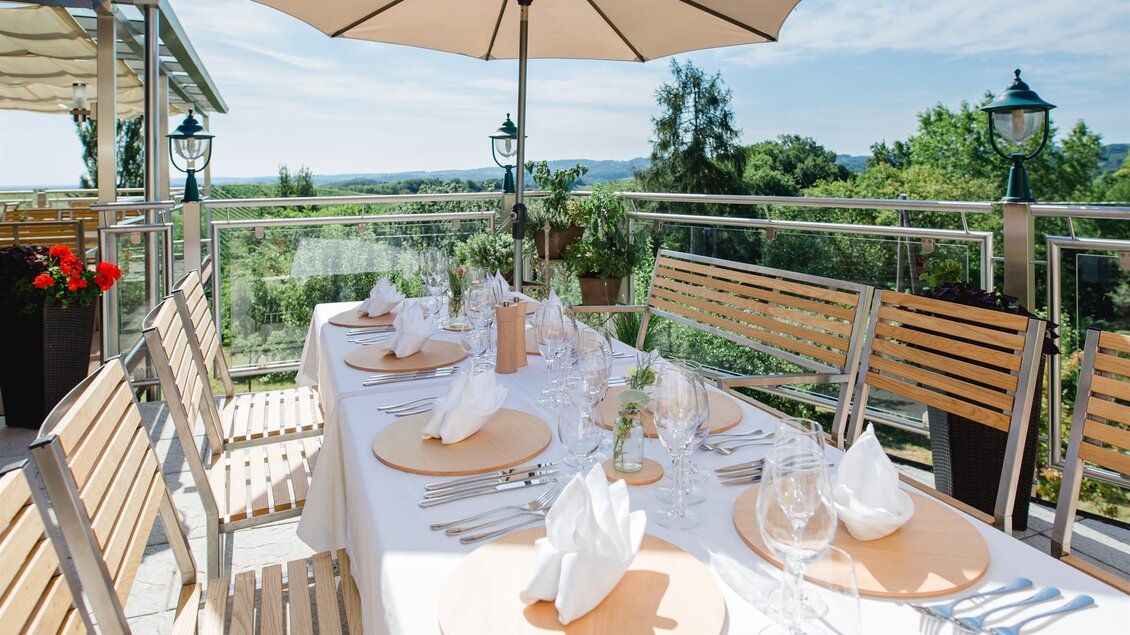 Ein hübsch eingedeckter Tisch im Freien mit Sonnenschirm. Die Umgebung bietet eine schöne Aussicht auf die Natur. | © Tinnauer