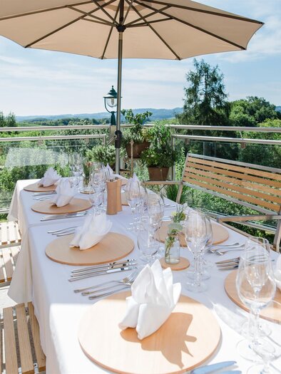 Ein hübsch eingedeckter Tisch im Freien mit Sonnenschirm. Die Umgebung bietet eine schöne Aussicht auf die Natur. | © Tinnauer