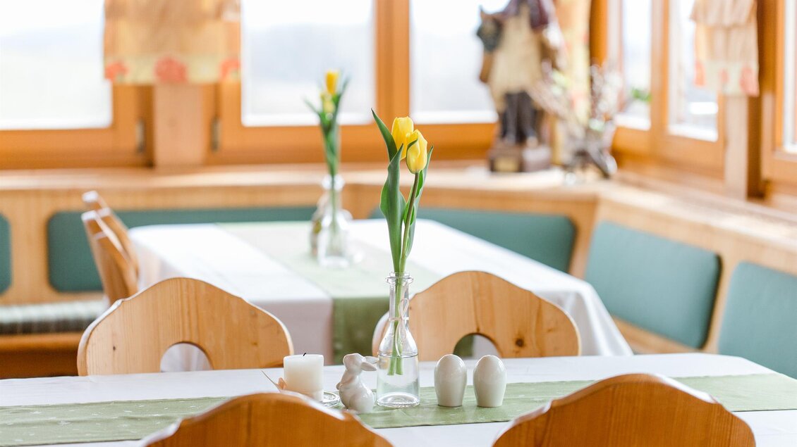 Ein einladendes Restaurant mit hellen Fenstern und Holzdekor. Auf den Tischen stehen frische Blumen und dekorative Elemente. | © Tinnauer