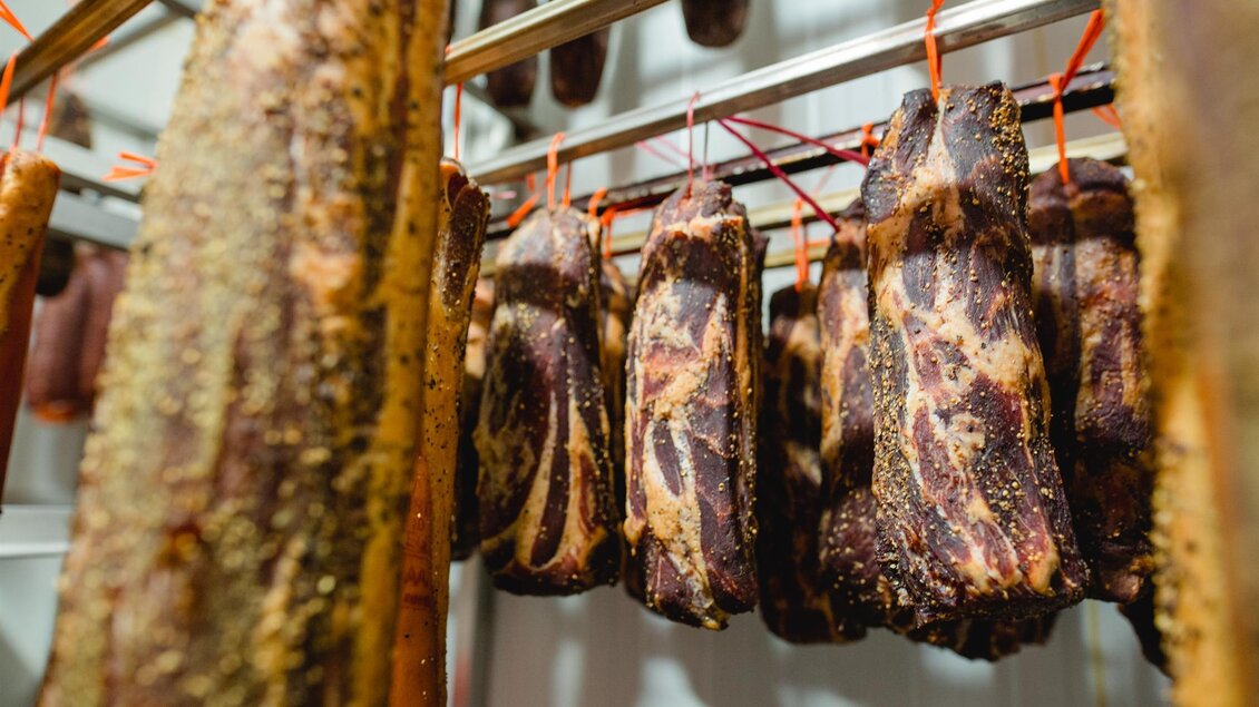 Eine Vielzahl von luftgetrocknetem Fleisch hängt in einem Kühlschrank. Die Farben und Texturen des Fleisches sind gut sichtbar. | © Tinnauer