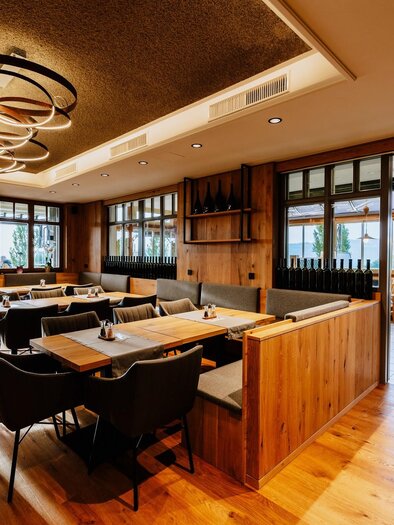 A modern restaurant with wooden interiors and comfortable seating. Large windows offer a nice view outside.