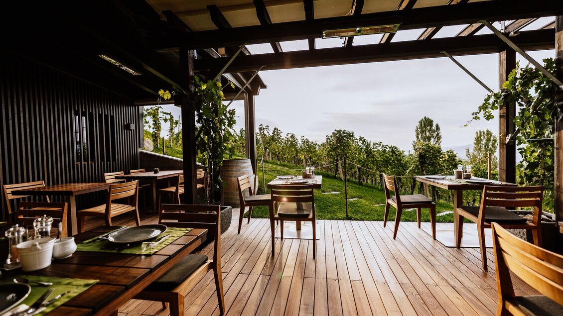 Ein modernes Restaurant mit Holzmöbeln und Blick auf eine grüne Landschaft. Große Fenster lassen viel Licht herein und bieten eine einladende Atmosphäre.