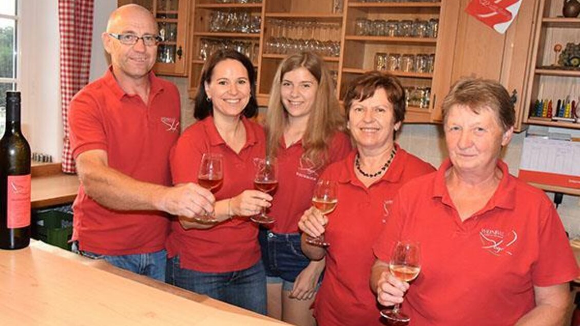 Eine Gruppe von fünf Personen steht hinter einer Theke und hält Gläser in der Hand. Alle tragen rote T-Shirts und lächeln freundlich.