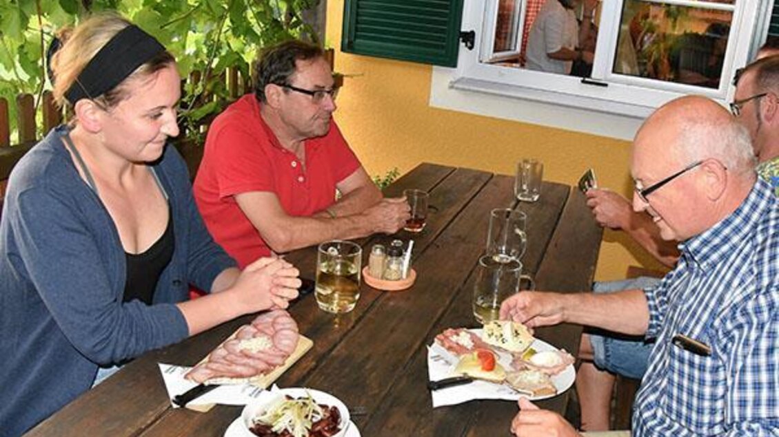Eine Gruppe von vier Personen sitzt an einem Tisch im Freien und genießt ein Essen. Auf dem Tisch sind verschiedene Gerichte und Getränke zu sehen.