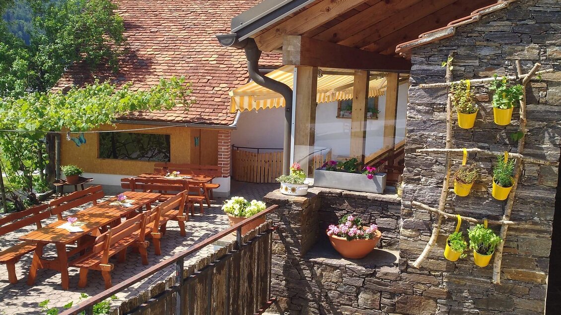 Ein malerisches Restaurant mit Holzterrasse und Bänken im Freien. Die Fassade ist mit Pflanzen dekoriert und es gibt einen schönen Blick auf die Umgebung. | © Peter Preu