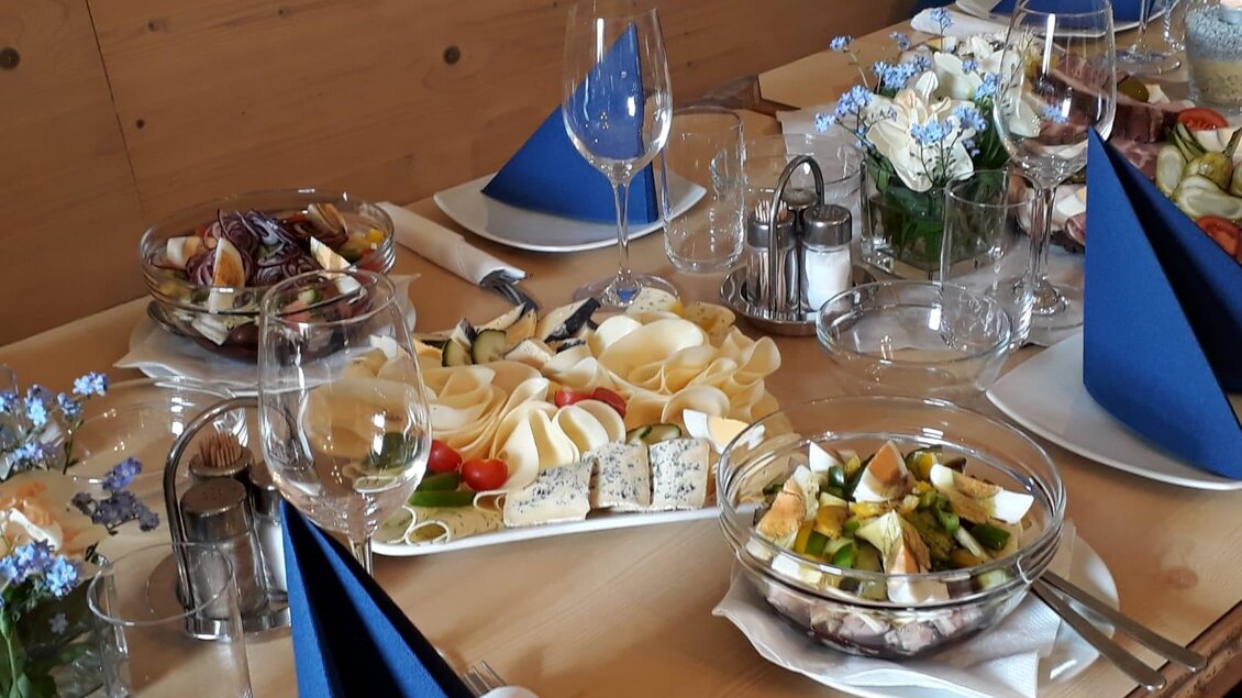 Ein schön gedeckter Tisch mit verschiedenen Salaten, Käsesorten und Obst. Blue Tischdecken und Gläser ergänzen die dekorative Atmosphäre. | © Andreas Wutti | Weingut Buschenschank Wutti