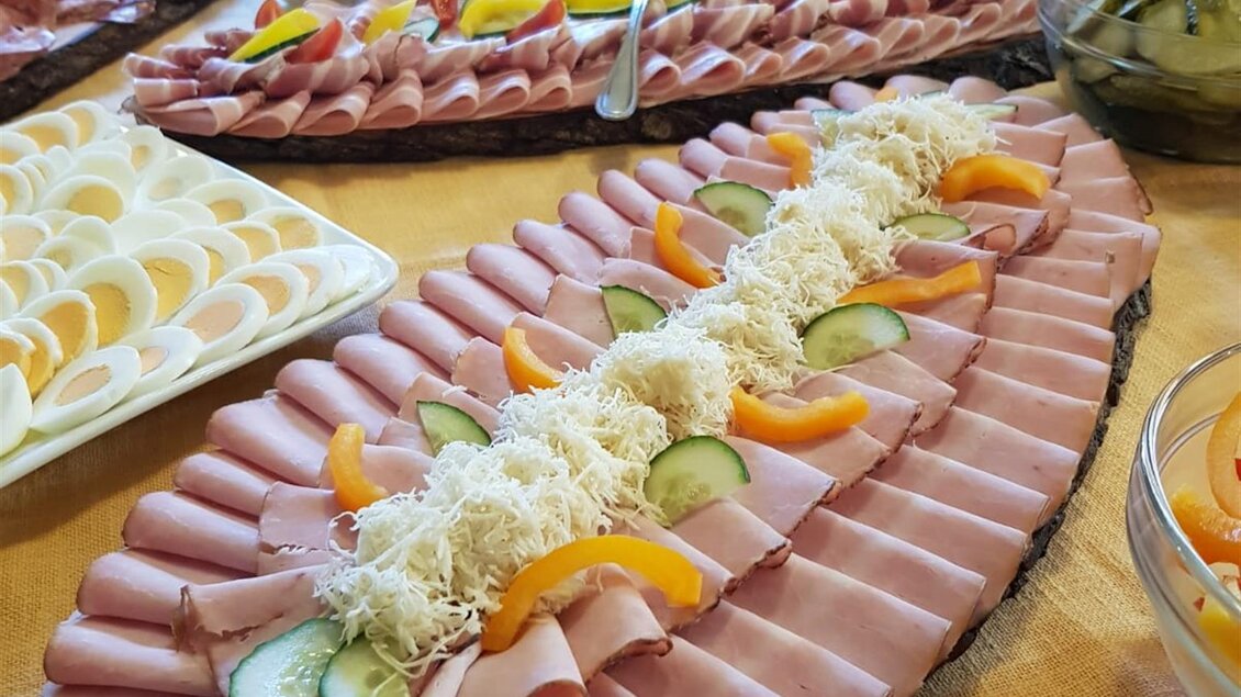 Ein reichhaltiges Buffet mit aufwendig angerichtetem Aufschnitt, dekoriert mit Gurken und Orangenscheiben. Im Hintergrund sind weitere Speisen und Salate zu sehen. | © Andreas Wutti | Weingut Buschenschank Wutti
