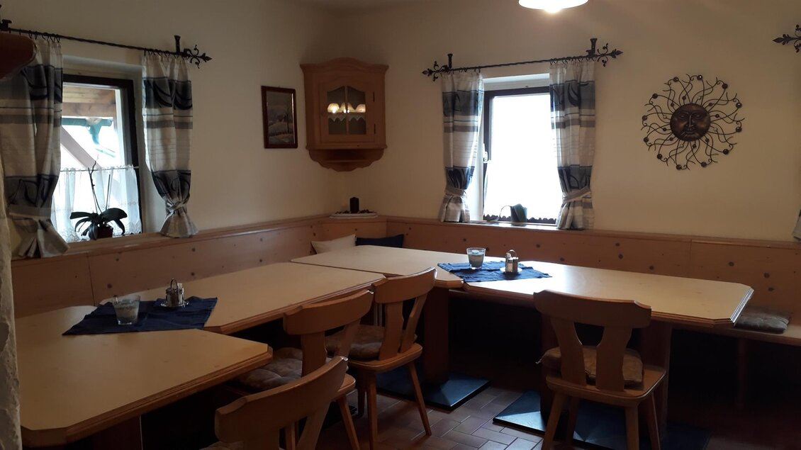 Ein gemütlicher Essbereich mit Holzstühlen und Tischen. Große Fenster lassen viel Licht herein und die Wände sind einfach dekoriert. | © Andreas Wutti | Weingut Buschenschank Wutti