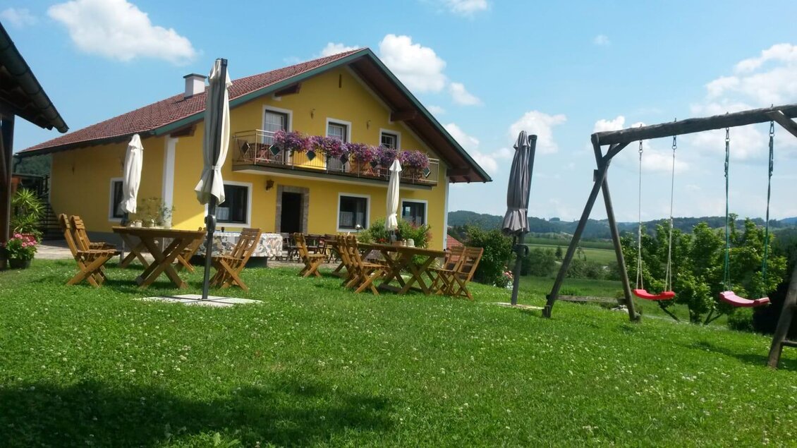Ein hübsches gelbes Haus mit einem großen Garten. Im Garten stehen Tisch und Stühle sowie eine Schaukel. | © Andreas Wutti | Weingut Buschenschank Wutti