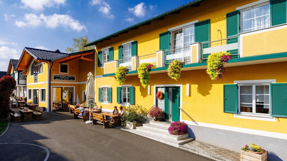 Bunte Gebäude mit grünen Fensterläden und Blumenampeln. Auf der Terrasse sitzen Gäste und genießen die Sonne. | © TV Region Graz - Harry Schiffer