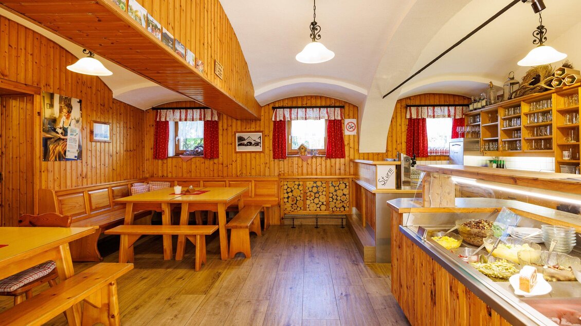 Ein gemütliches Café mit Holzverkleidung und warmem Ambiente. Die Einrichtung ist einladend mit Tischen, Bänken und einer Kuchenauslage. | © TV Region Graz - Harry Schiffer