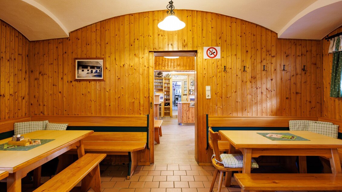 Ein gemütlicher Gastraum mit Holzvertäfelung und einfachen Tischen. Im Hintergrund ist eine Tür, die zu einer weiteren Räumlichkeit führt. | © TV Region Graz - Harry Schiffer