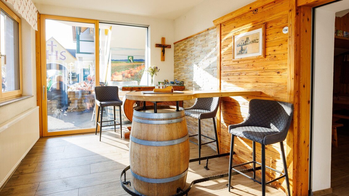 Ein gemütlicher Gastraum mit einem Holzbar und modernen Barstühlen. Viel Tageslicht strömt durch das große Fenster. | © TV Region Graz - Harry Schiffer