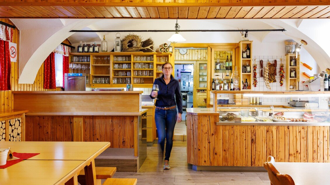 Eine gemütliche Restaurant-Atmosphäre mit Holzmöbeln und einem freundlich lächelnden Servicepersonal. Im Hintergrund sind Regale mit Getränken und traditionellen Lebensmitteln sichtbar. | © TV Region Graz - Harry Schiffer
