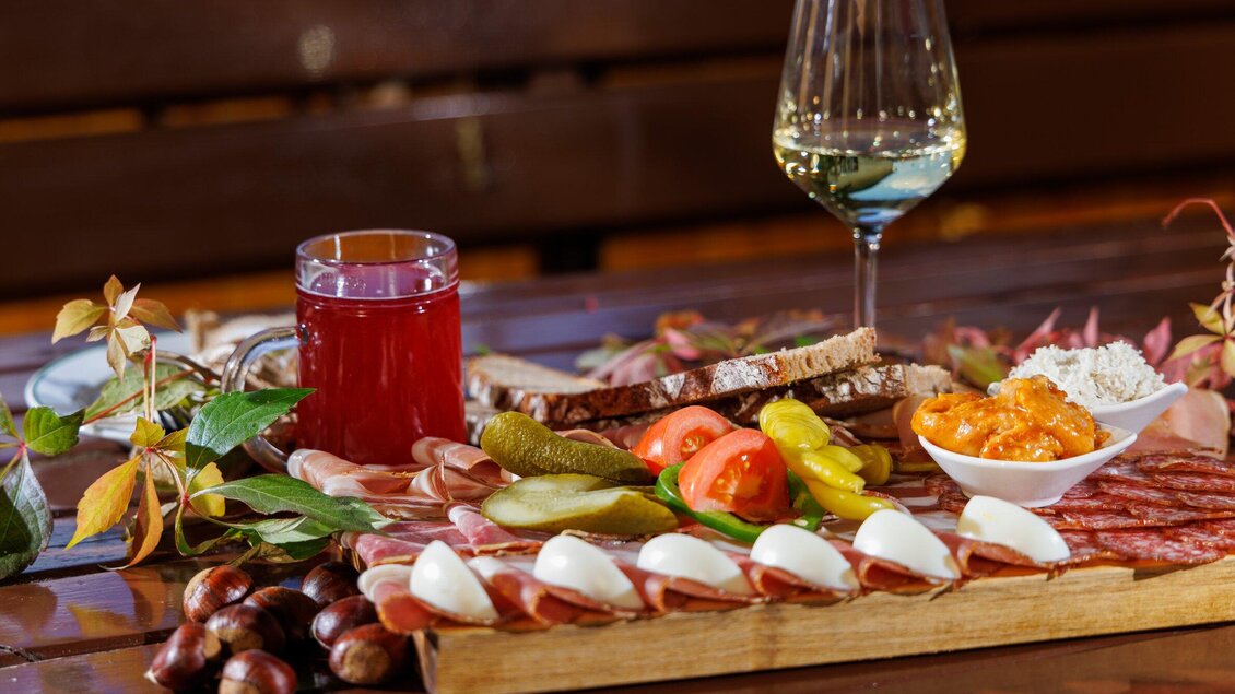 Ein üppiges Brett mit Wurst, Käse, frischem Gemüse und Brot. Dazu ein Glas Weißwein und ein Getränk. | © TV Region Graz - Harry Schiffer