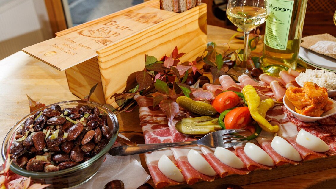 Ein reichhaltiges Platte mit Wurst, Käse, Gurken und Paprika. Dazu ein Glas Wein und eine Schale mit Bohnen. | © TV Region Graz - Harry Schiffer