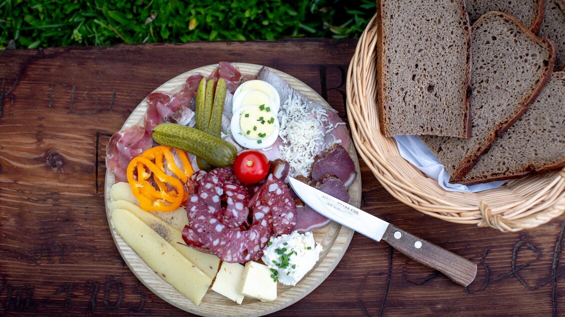 Ein Teller mit verschiedenen Wurst- und Käsesorten, eingelegten Gurken und einem kleinen Salat. Daneben liegt ein Korb mit frischem Brot. | © TV Murau