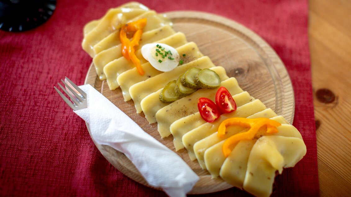 Ein Holzbrett mit verschiedenen Käsescheiben, garniert mit buntem Gemüse. Daneben liegt eine Serviette und eine Gabel. | © TV Murau