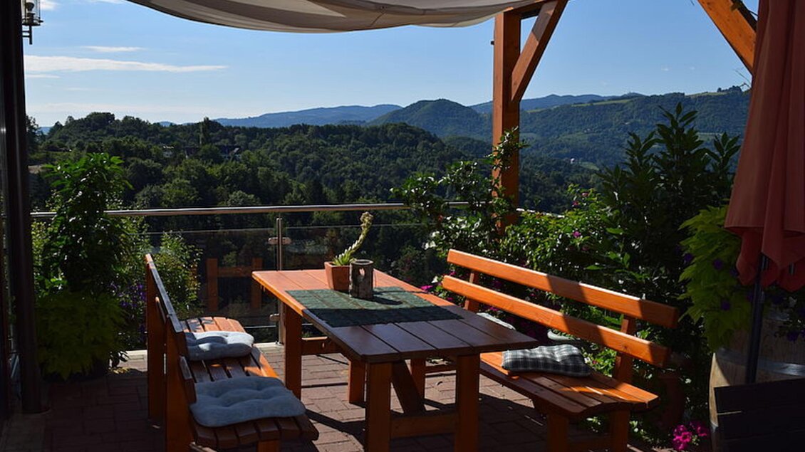 Eine gemütliche Terrasse mit einem Holztisch und Bänken. Im Hintergrund sind grüne Hügel und Bäume zu sehen. | © Walter Christian Zitz | Weinhof Zitz