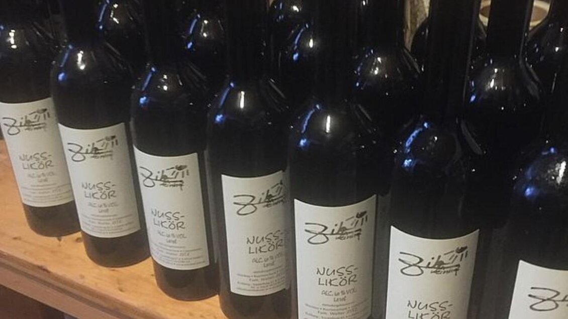 Eine Reihe von schwarzen Weinflaschen mit hellen Kapseln steht ordentlich auf einem Regal. Die Etiketten zeigen den Namen des Weins und die Abbildung ist ansprechend und einladend. | © Walter Christian Zitz | Weinhof Zitz