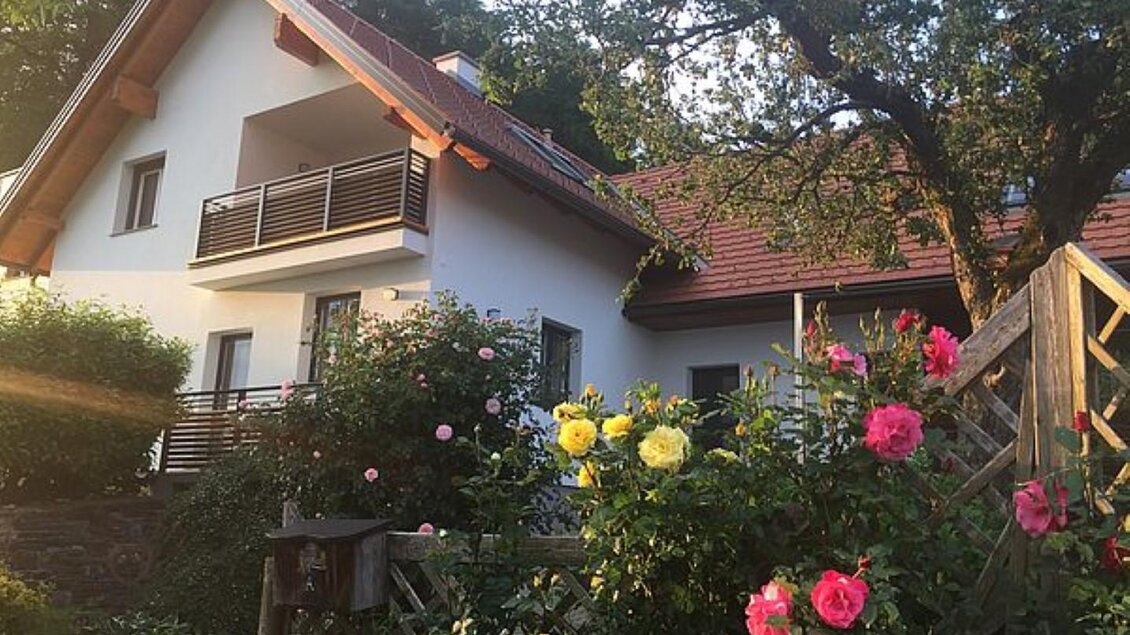 Ein schönes Haus mit einem roten Dach und Balkon. Bunte Rosen blühen im Vordergrund. | © Walter Christian Zitz | Weinhof Zitz