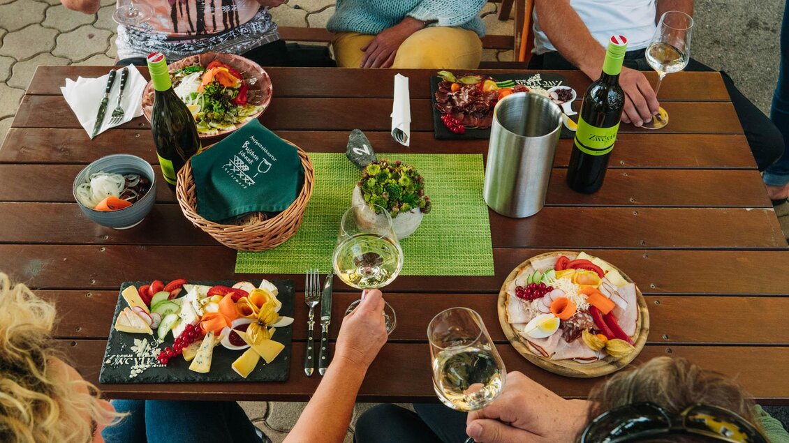 Ein gedeckter Tisch mit verschiedenen Gerichten, darunter Käse, Obst und Salate. Gläser mit Wein und Bier ergänzen das appetitliche Menü. | © Weingut & Buschenschank Zweytick | Fam. Zweytick