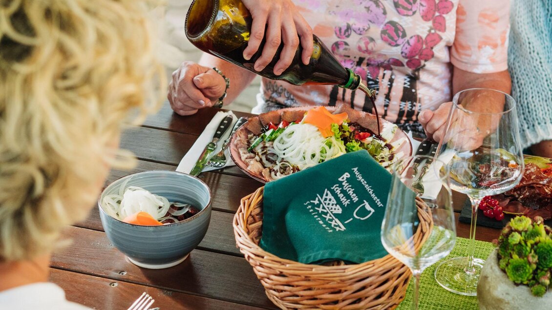 Ein gemütliches Essen am Tisch mit frischem Salat und Wein. Eine Person gießt Olivenöl über einen Teller mit Gemüse. | © Weingut & Buschenschank Zweytick | Fam. Zweytick