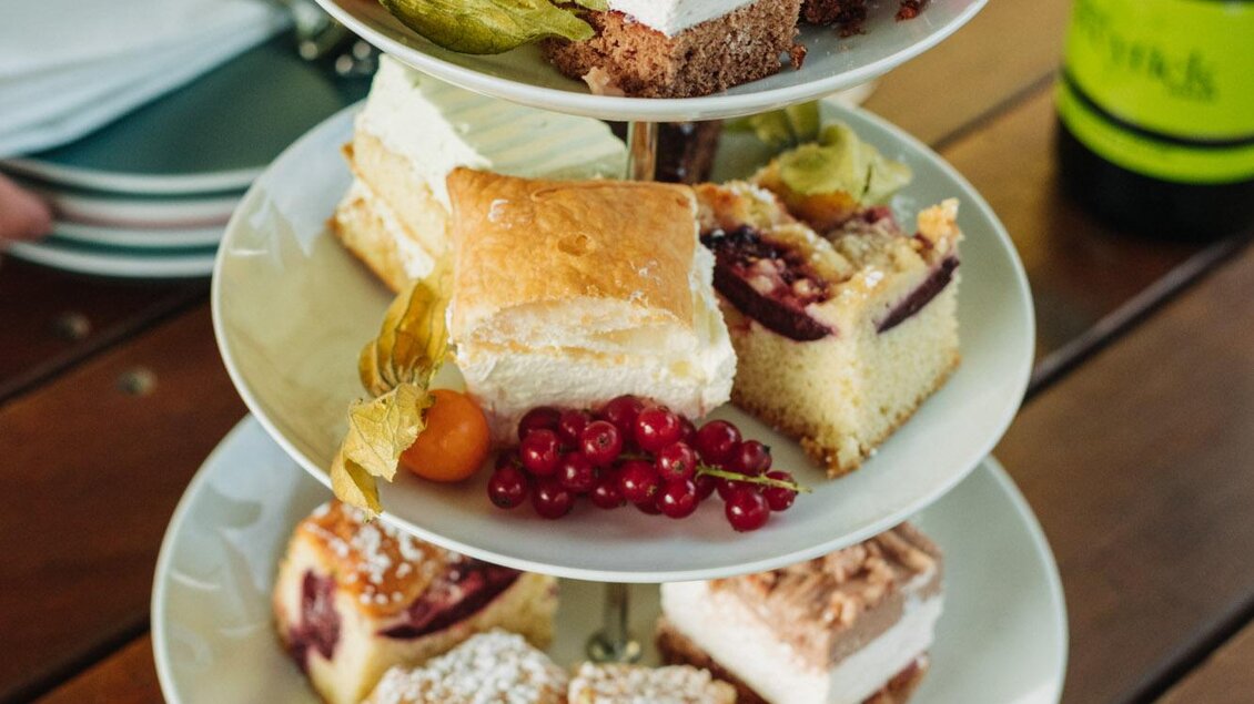 Eine elegante Tortenplatte mit verschiedenen köstlichen Desserts und frischen Früchten. Im Hintergrund steht eine Flasche Wein. | © Weingut & Buschenschank Zweytick | Fam. Zweytick