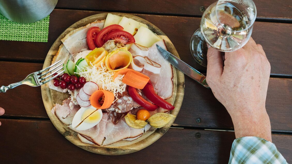 Ein liebevoll angerichteter Teller mit verschiedenen Aufschnittsorten, frischem Gemüse und Obst. Daneben steht ein Glas Wasser. | © Weingut & Buschenschank Zweytick | Fam. Zweytick