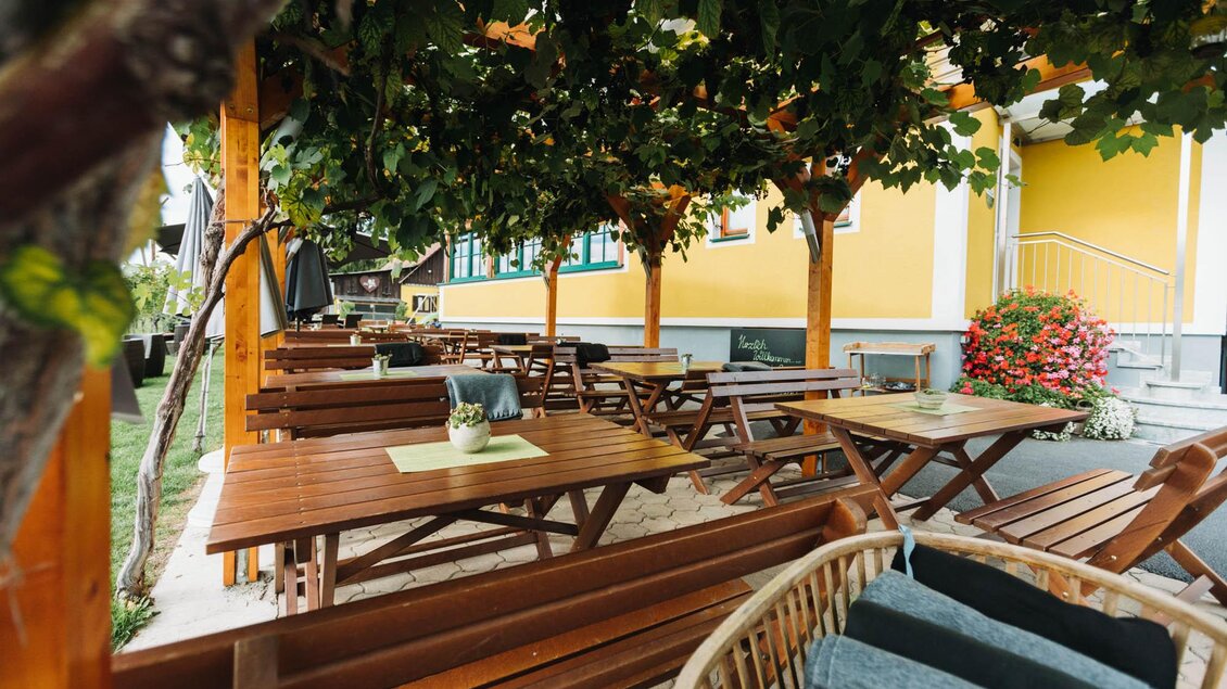 Ein gemütlicher Außenbereich mit Holzmöbeln und schattenspendenden Pflanzen. Die Umgebung ist freundlich und einladend, ideal zum Entspannen. | © Weingut & Buschenschank Zweytick | Fam. Zweytick