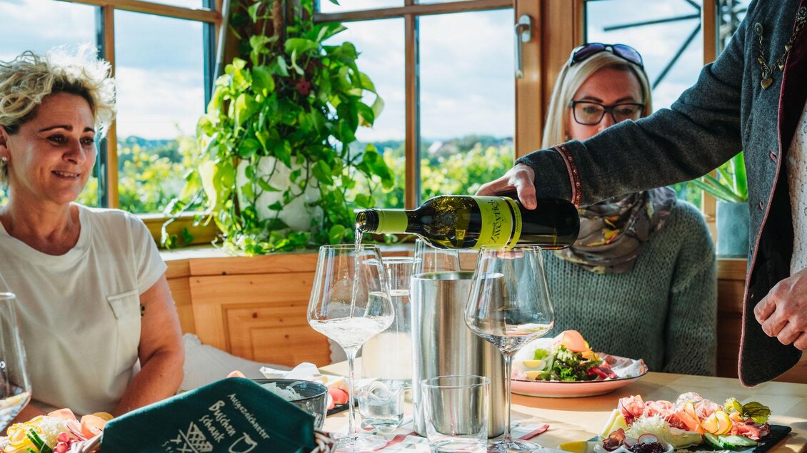 Eine gemütliche Tafel mit mehreren Gläsern und einem Weinflaschenservice. Im Hintergrund sieht man frisches Essen und eine grüne Pflanzenkulisse. | © Weingut & Buschenschank Zweytick | Fam. Zweytick