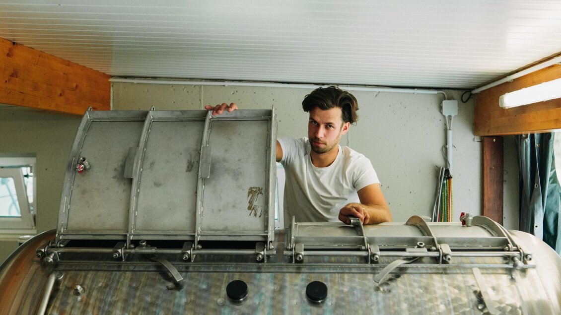 Ein Mann arbeitet an einem großen Metallbehälter in einem Innenraum. Er überprüft die Teile des Behälters sorgfältig. | © Weingut & Buschenschank Zweytick | Fam. Zweytick