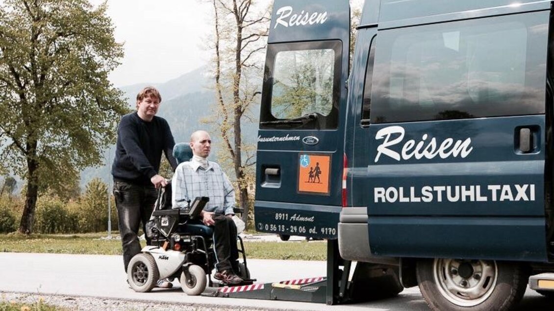 Ein Rollstuhltaxi ist an einer Straße geparkt. Eine Person hilft einem Mann im Rollstuhl, in das Taxi einzusteigen. | © Stefan Leitner