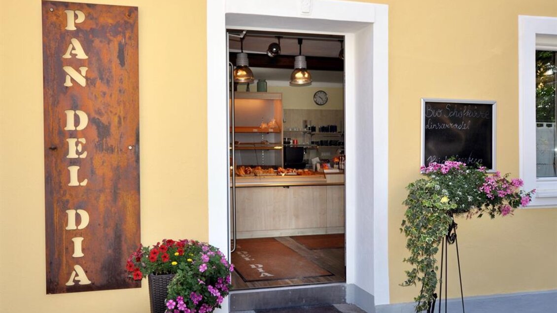 Ein einladender Eingang zu einer Bäckerei mit dem Namen "Pan del Dia". Blumen in Töpfen schmücken die Tür und schaffen eine freundliche Atmosphäre. | © Sabine Pauritsch
