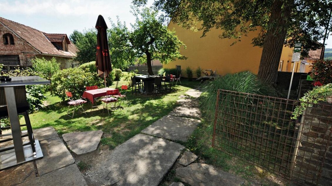 Ein einladender Garten mit Tischen und Stühlen, umgeben von grünen Bäumen. Der Weg ist mit Natursteinen gepflastert und führt zu einem ruhigen Outdoor-Bereich. | © Sabine Pauritsch