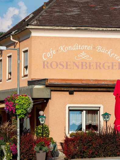 Ein gemütliches Café mit der Aufschrift "Rosenberger". Es ist von bunten Blumen und sonnigem Wetter umgeben. | © TV Region Graz - Harry Schiffer