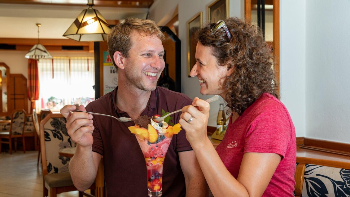 Ein glückliches Paar genießt ein großes Dessert mit frischem Obst in einem gemütlichen Restaurant. Sie lächeln sich an und teilen einen Moment der Freude. | © TV Region Graz - Harry Schiffer